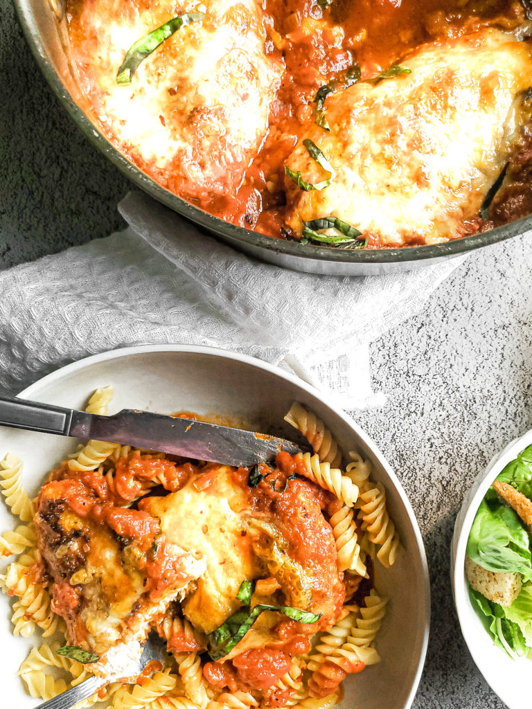 Chicken parmesan in a skillet with a serving in a bowl with pasta